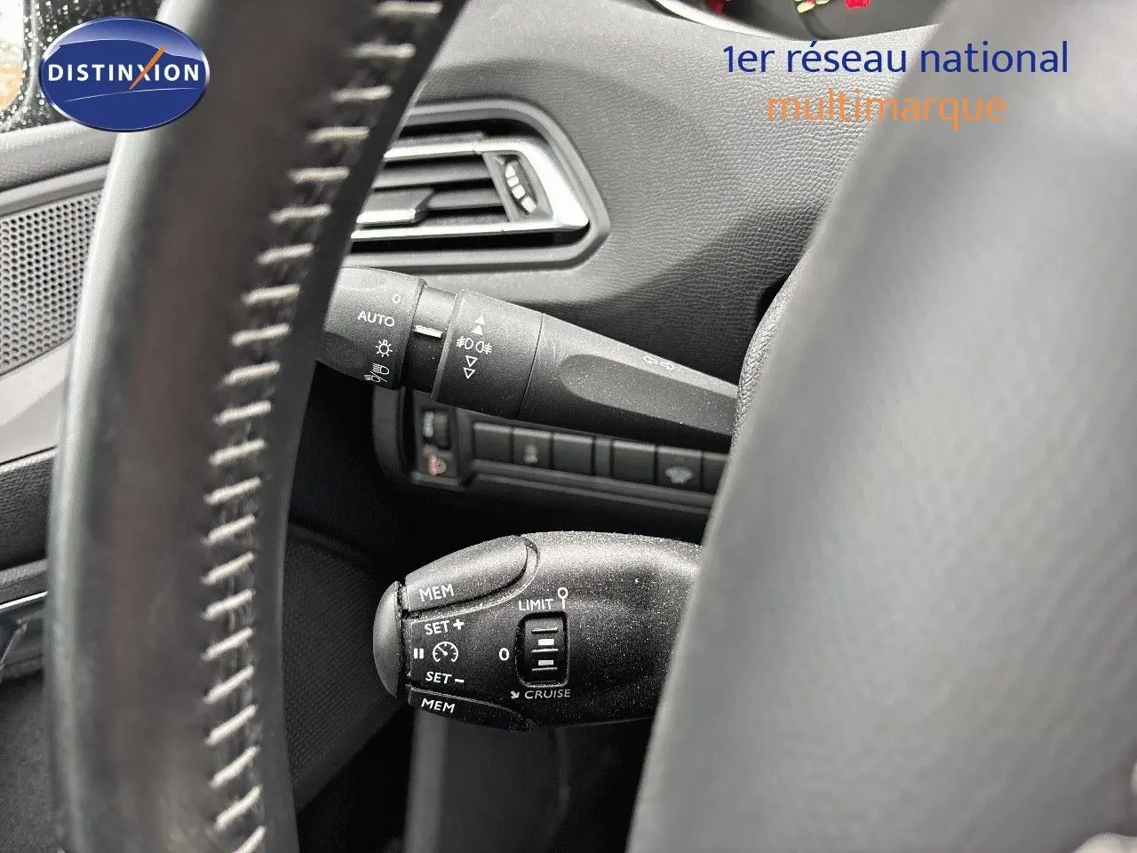 Gros plan sur la commande de régulateur de vitesse derrière le volant d'une Peugeot 308 gris Artense, intérieur noir.