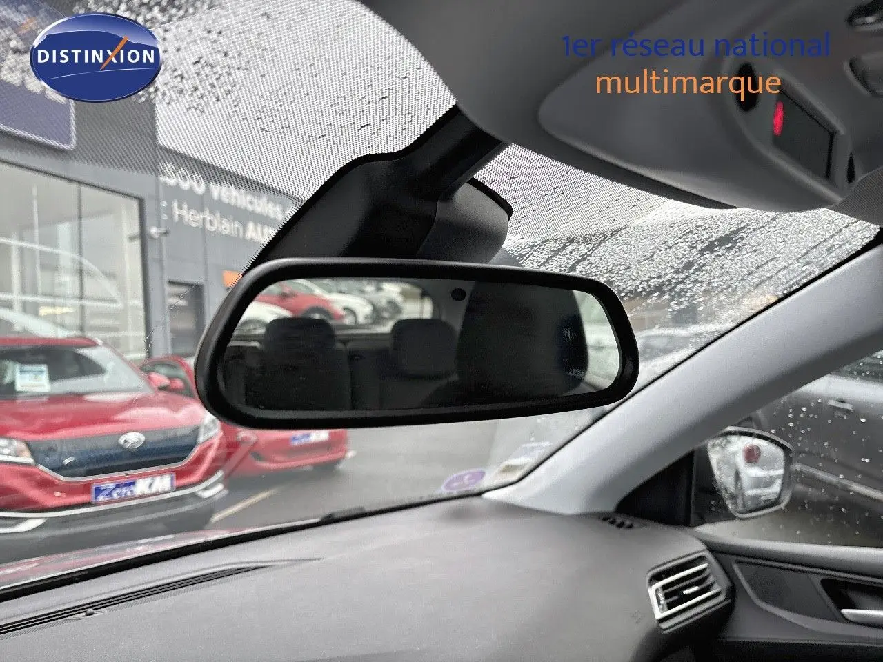 Vue intérieure du rétroviseur central d'une Peugeot 308 gris Artense, avec tableau de bord et pluie sur le pare-brise visible.