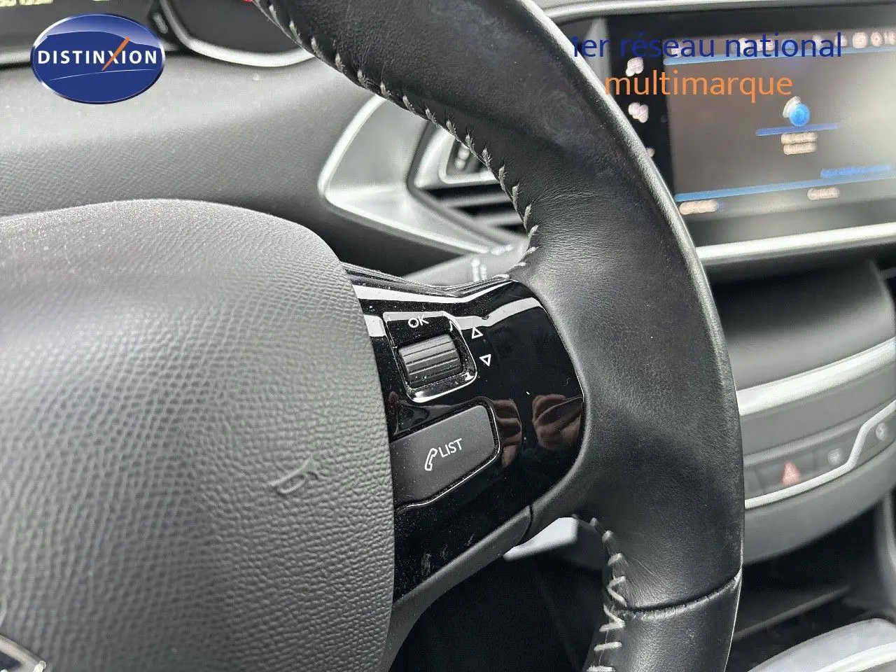 Gros plan sur le volant en cuir noir de la Peugeot 308 gris Artense, avec commandes intégrées visibles côté gauche.