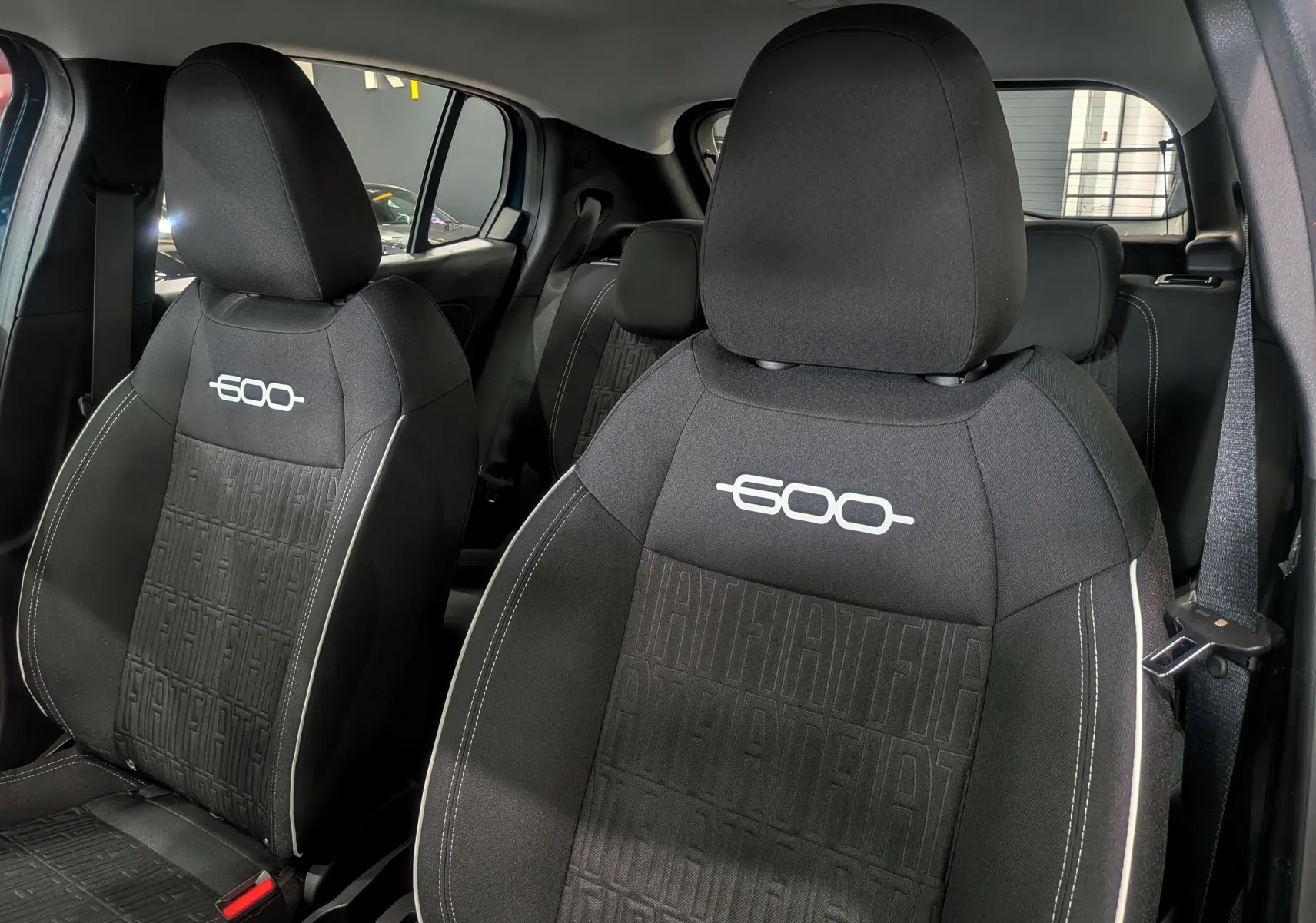 Gros plan sur les sièges avant noirs avec logo 600 blanc et motifs FIAT en relief dans l'habitacle d'une FIAT 600 bleu Sea.