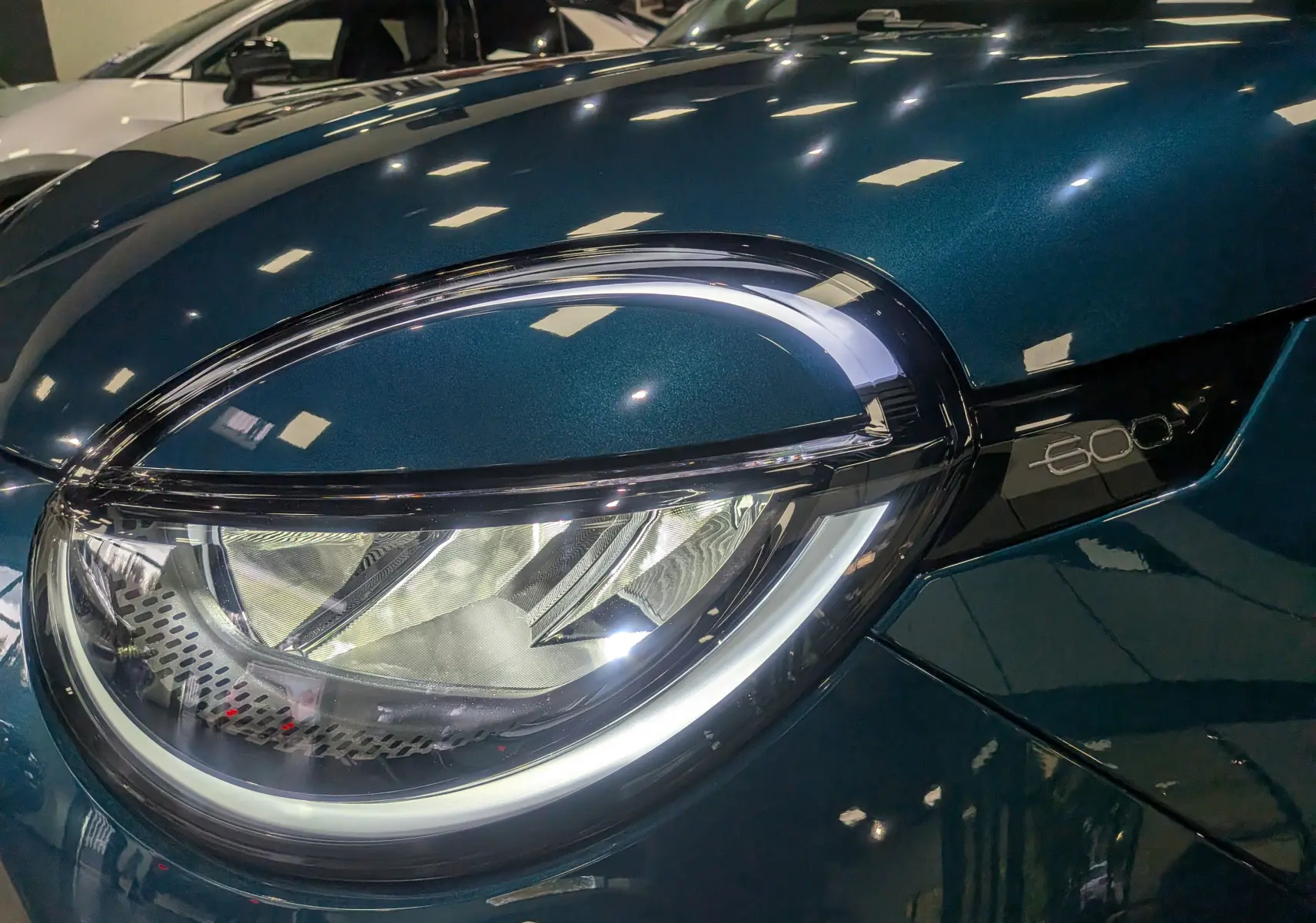 Gros plan sur le phare avant droit bleu Sea du Fiat 600 1.2 Hybrid 145 CH eDCT6 POP avec logo 600 visible.