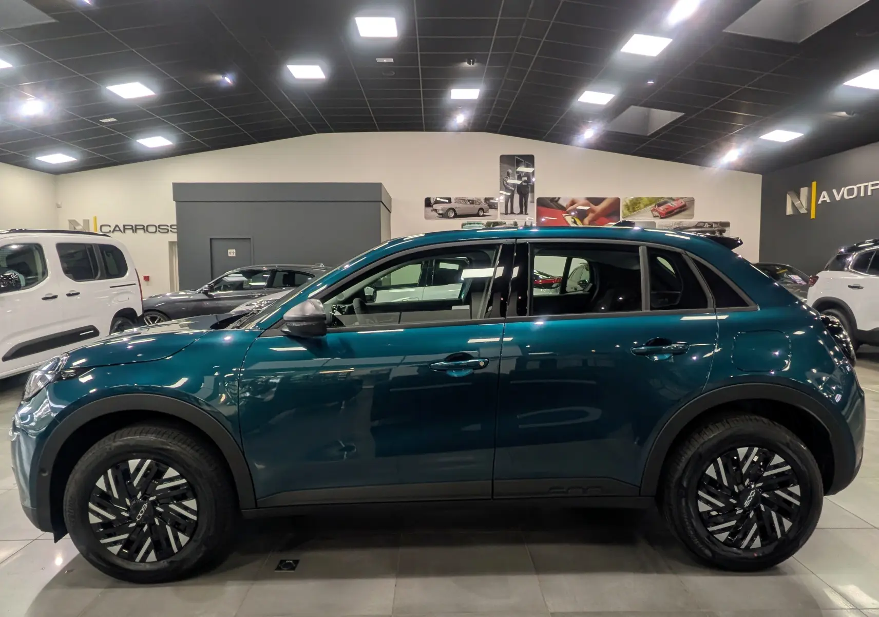 Vue de profil côté gauche d'une FIAT 600 1.2 Hybrid bleu Sea en showroom, soulignant ses jantes noires et son design compact.