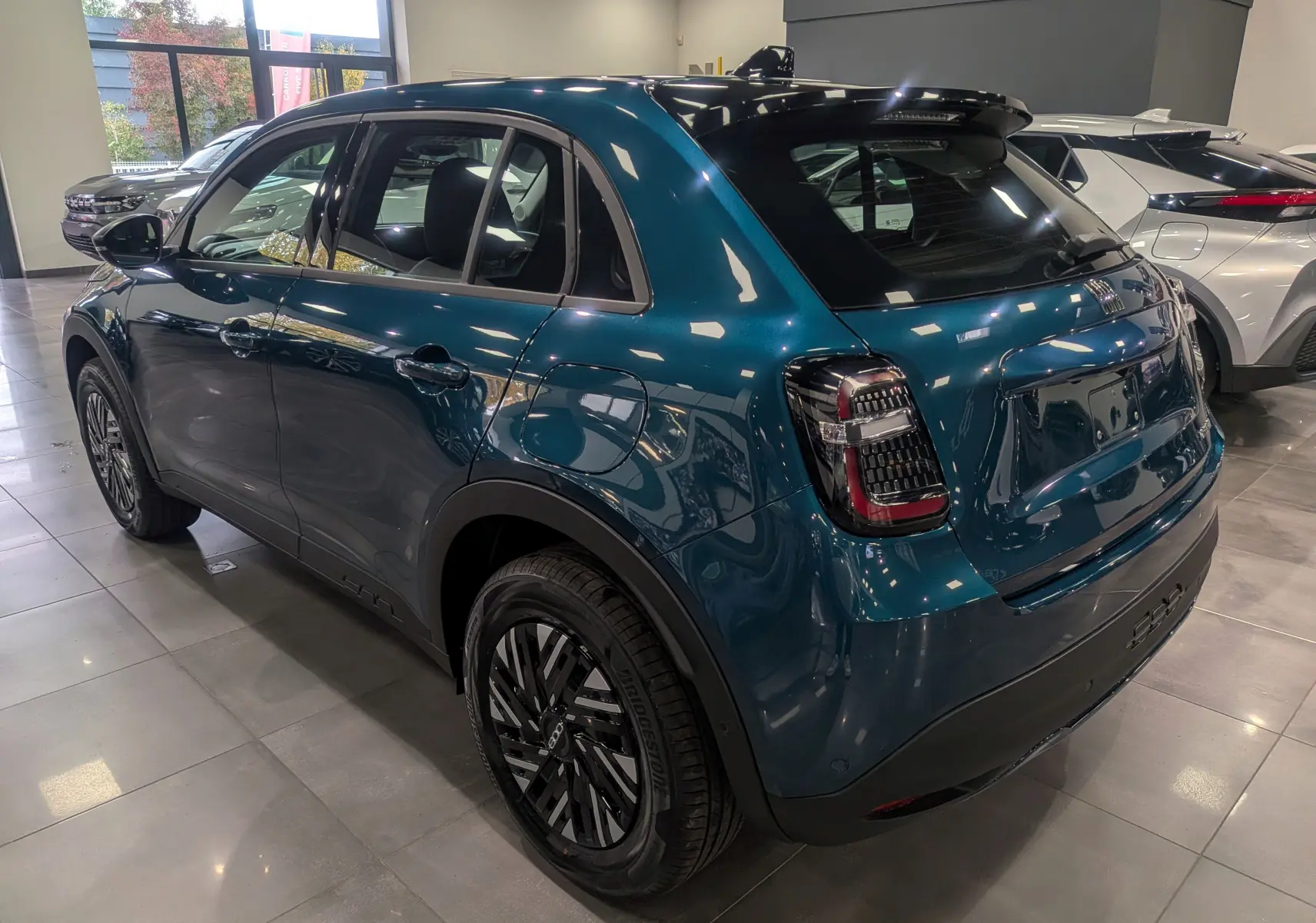 Vue 3/4 arrière droite d'une FIAT 600 1.2 Hybrid bleu Sea avec feux arrière noirs et jantes stylisées en concession.