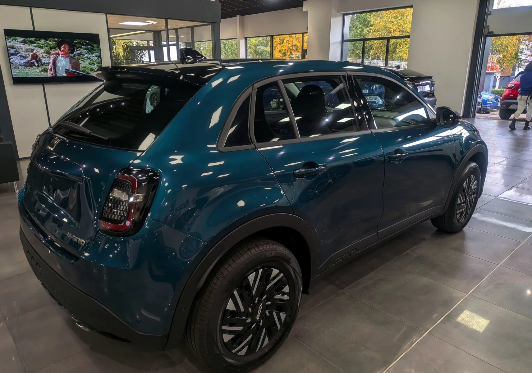 Vue 3/4 arrière droite d'une FIAT 600 hybride bleu Sea en showroom, avec jantes noires et toit noir brillant.