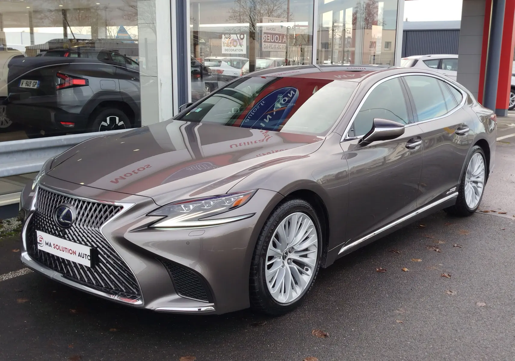 Lexus LS 500H gris manganèse en 3/4 avant, avec calandre distinctive et jantes multi-branches visibles.