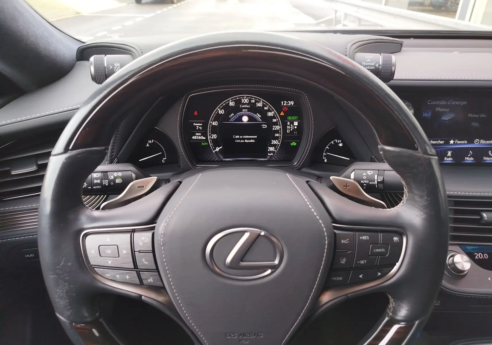 Vue intérieure centrée sur le volant cuir noir et le tableau de bord numérique de la Lexus LS 500H gris manganèse.