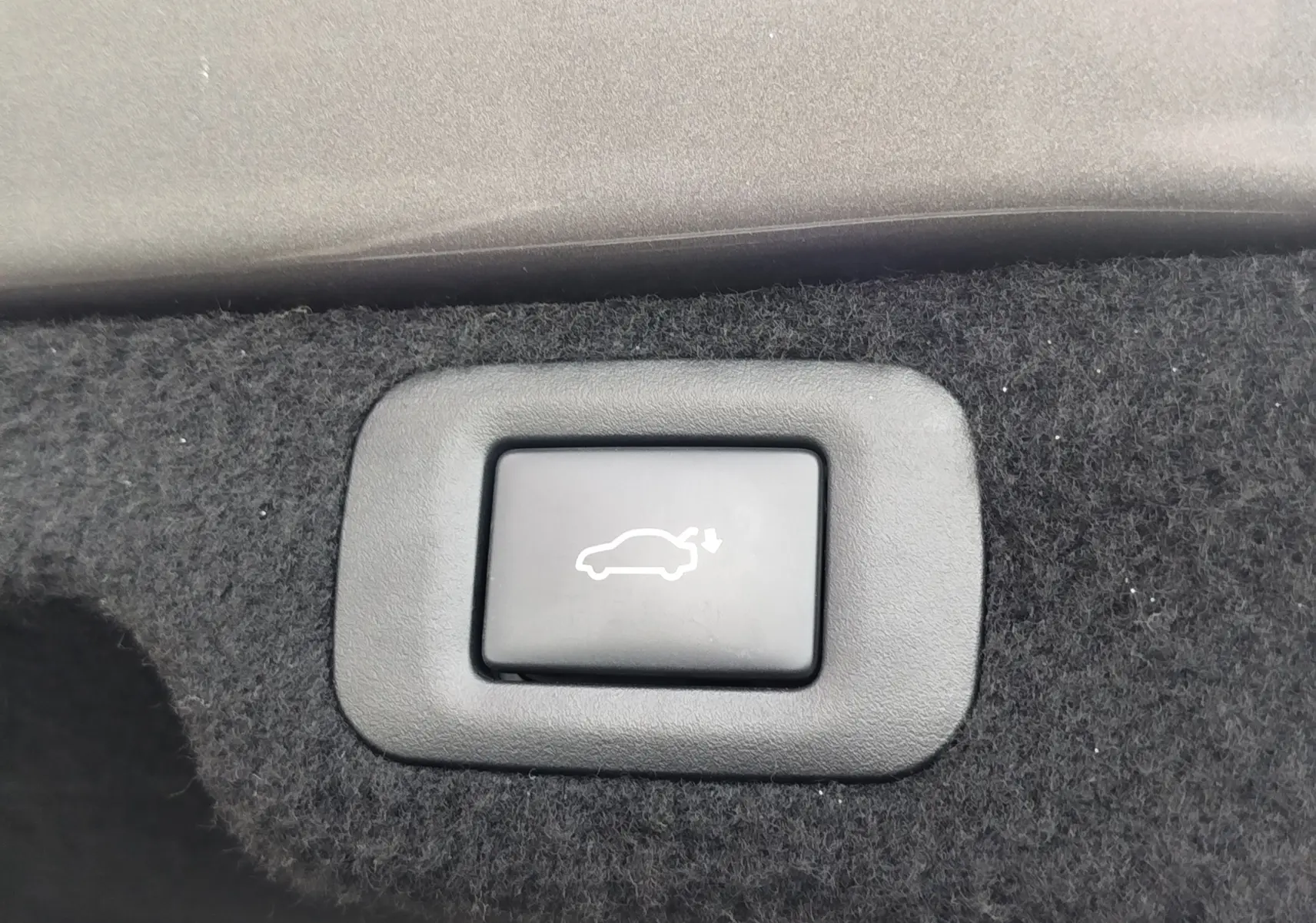 Bouton noir d'ouverture électrique du coffre sur revêtement intérieur en tissu gris foncé, détail du Lexus LS 500H.