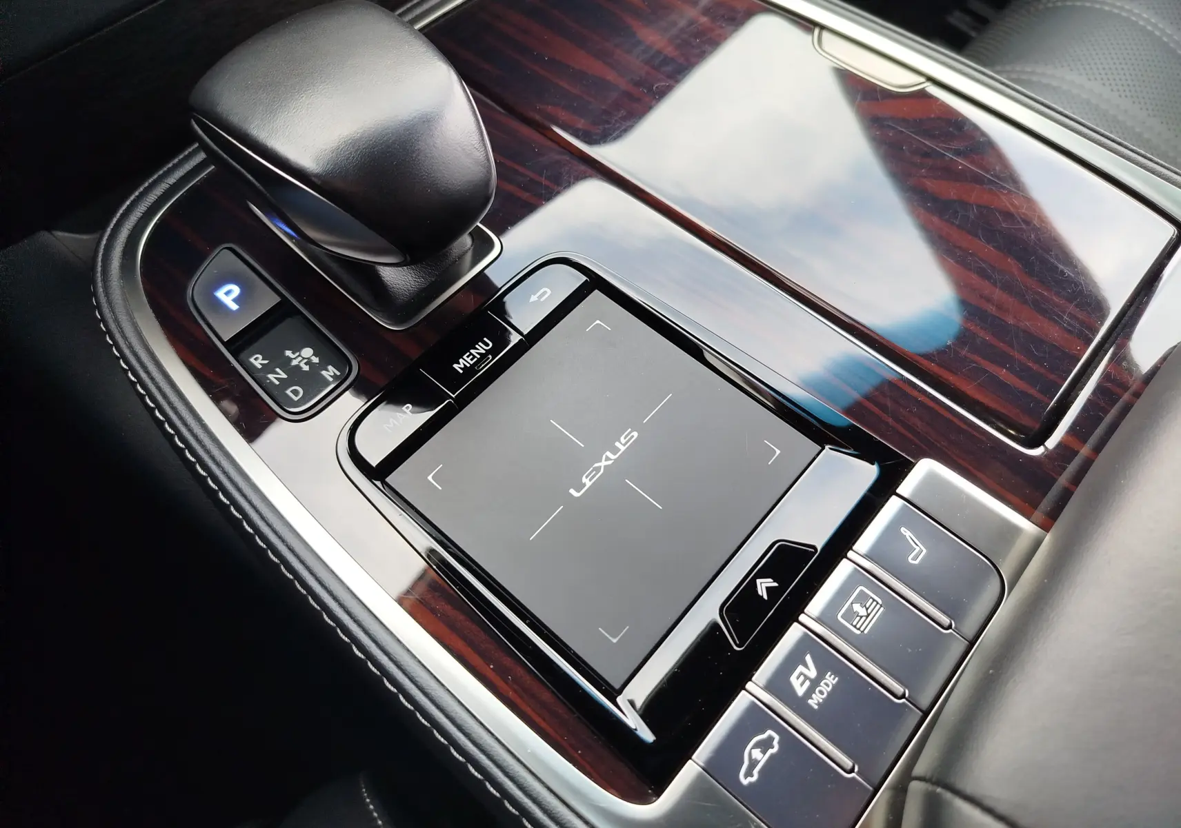 Gros plan sur la console centrale en bois brillant de la Lexus LS 500H 2020, avec levier de vitesse et pavé tactile Lexus.