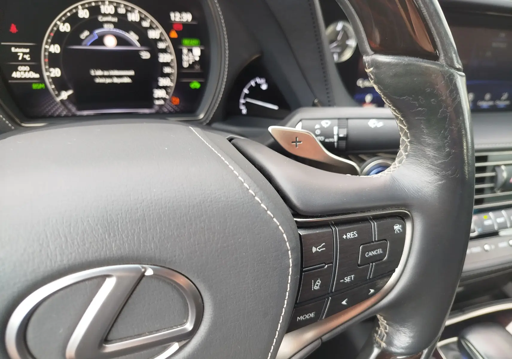 Gros plan sur le volant en cuir noir de la Lexus LS 500H 2020, avec commandes intégrées et tableau de bord numérique en arrière-plan.