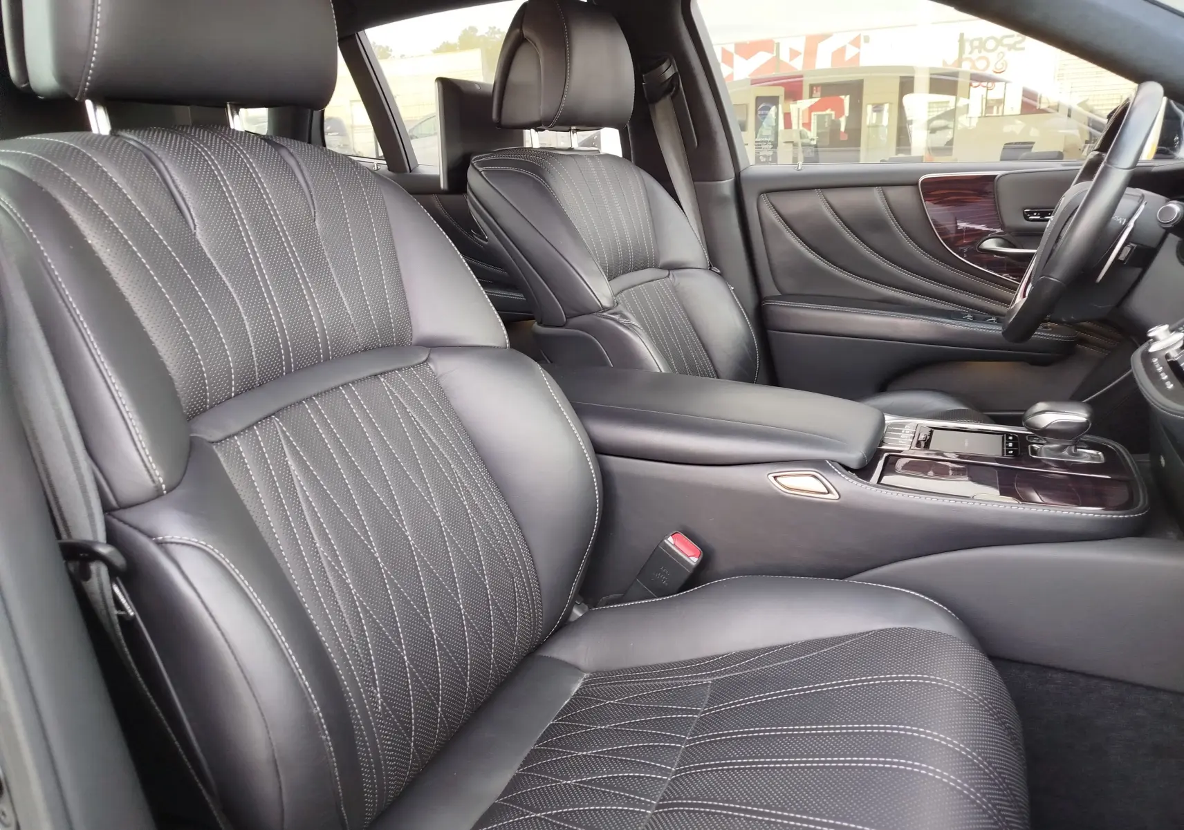 Vue intérieure côté conducteur de la Lexus LS 500H 2020, sièges cuir noir avec surpiqûres et inserts bois sur la porte.