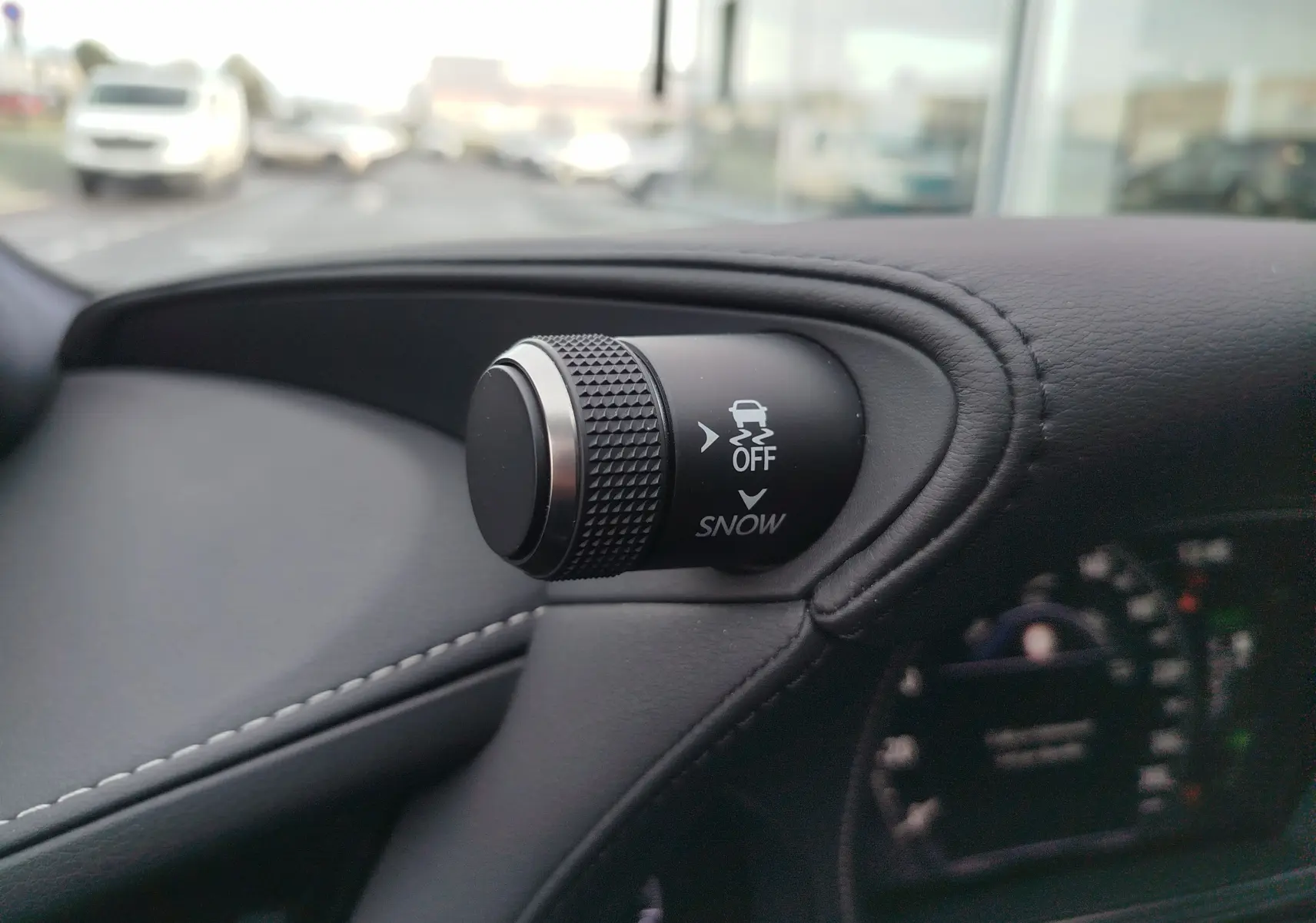 Gros plan sur le bouton de contrôle de traction et mode neige, sur tableau de bord en cuir noir du Lexus LS 500H gris manganèse.