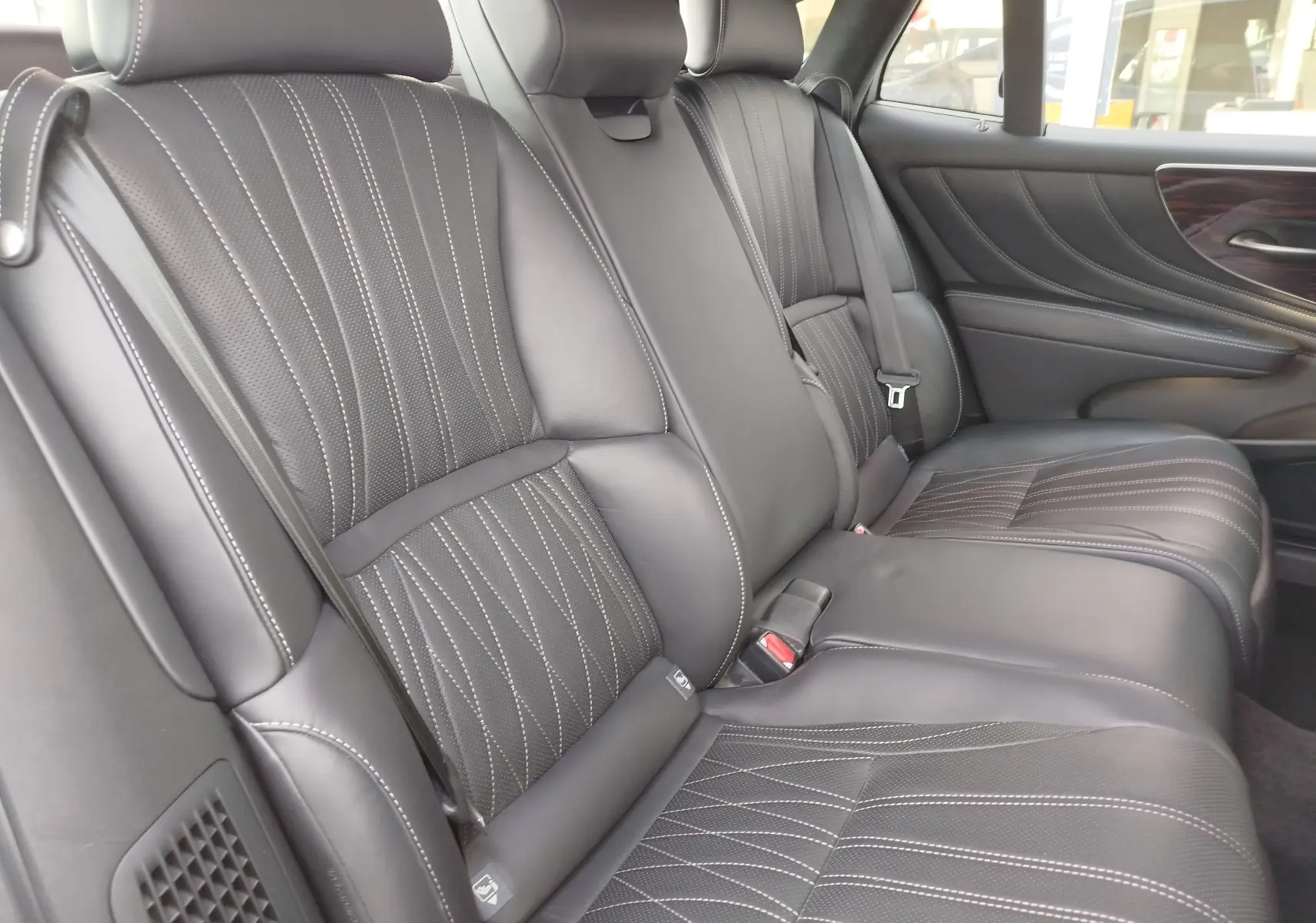 Vue intérieure des sièges arrière en cuir noir avec surpiqûres blanches et garnitures bois sur la porte d’une Lexus LS 500H.