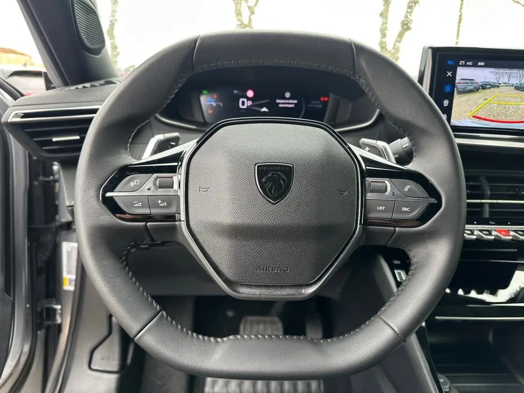 Vue rapprochée du volant cuir noir du Peugeot 2008 Hybrid 145 e-DCS6 Allure 2025 avec tableau de bord numérique et écran tactile.