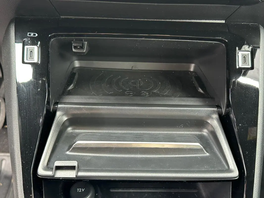 Gros plan sur la console centrale noire du Peugeot 2008 Hybrid 145, montrant le compartiment de recharge sans fil et ports USB.