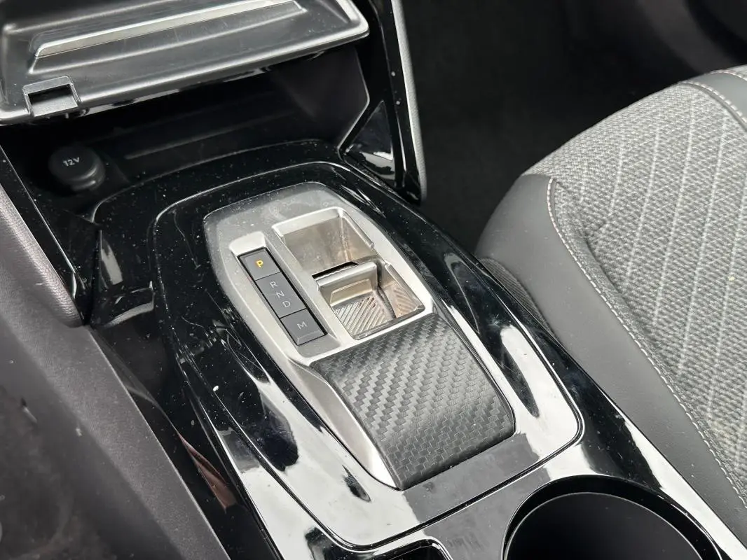 Vue rapprochée de la console centrale noire brillante avec levier de vitesse automatique et siège gris à motifs du Peugeot 2008 Hybrid 145.