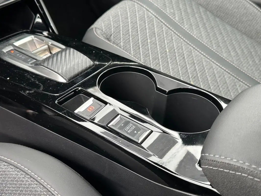 Gros plan sur la console centrale noire brillante du Peugeot 2008 Hybrid 145 Allure avec commandes de frein à main et mode de conduite.