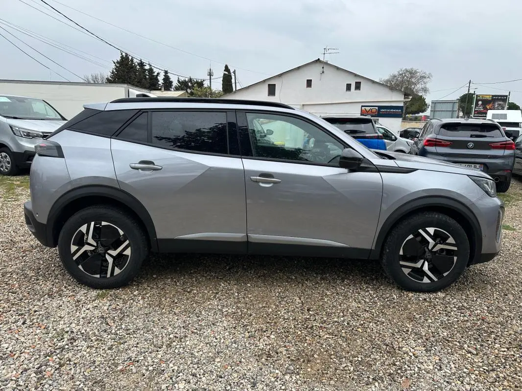 Profil côté gauche du Peugeot 2008 Hybrid 145 e-DCS6 Allure gris avec jantes alliage 17 pouces sur sol gravillonné.