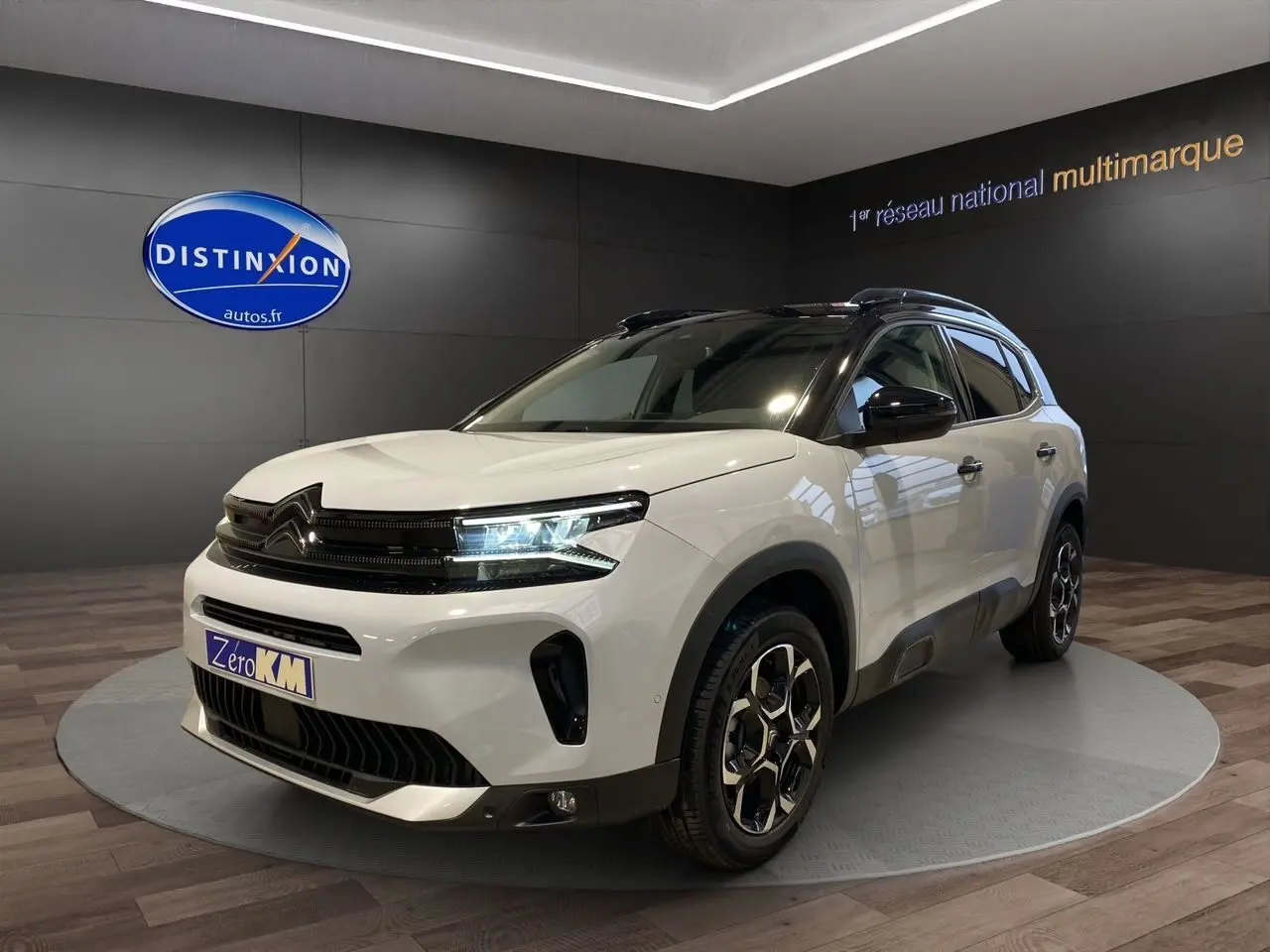 Vue 3/4 avant d'un Citroën C5 Aircross blanc avec toit noir et jantes alliage, en showroom intérieur.