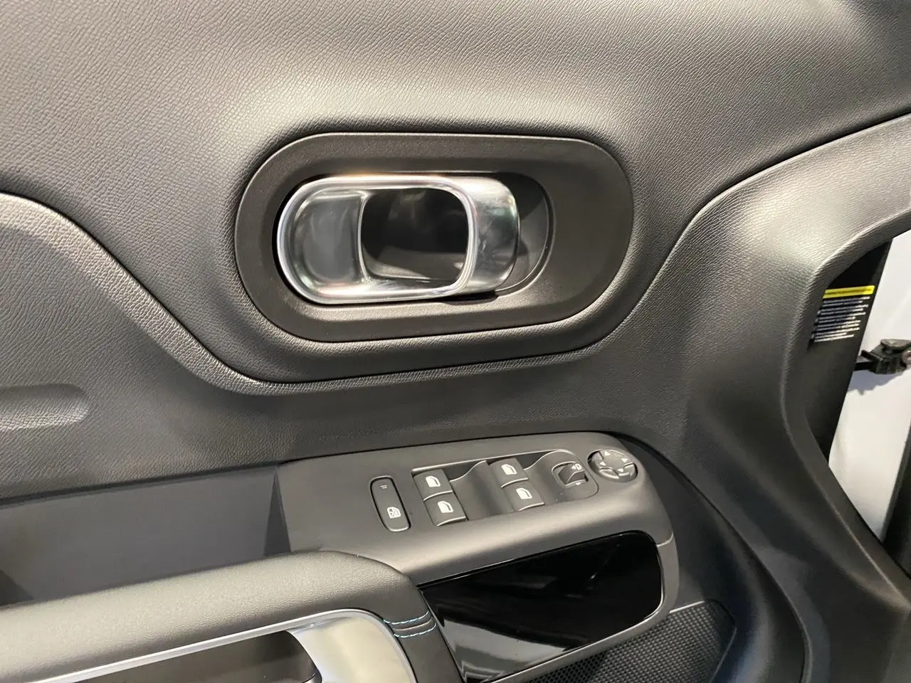 Poignée de porte intérieure côté conducteur en plastique noir avec commandes électriques sur une Citroën C5 Aircross blanc et noir.