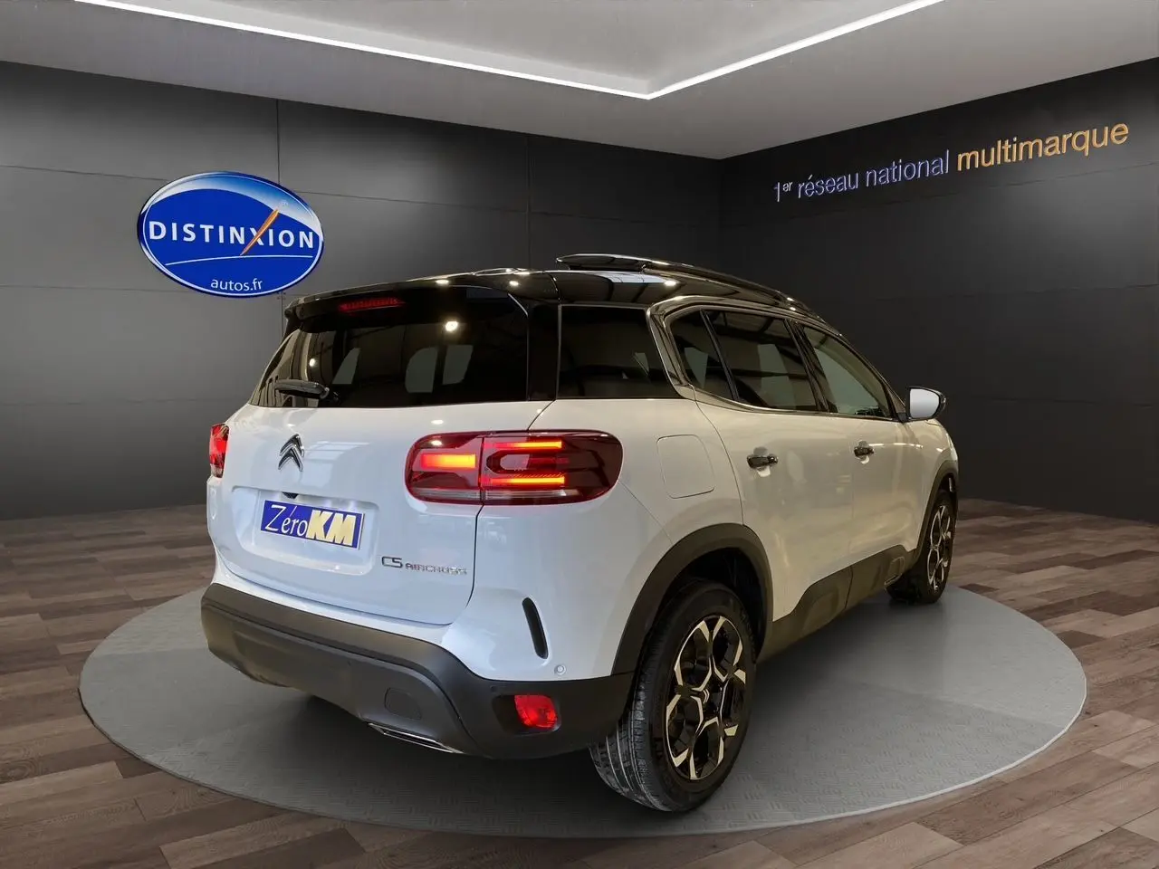 Vue 3/4 arrière droite d'un Citroën C5 Aircross blanc avec toit noir et feux arrière allumés en showroom.