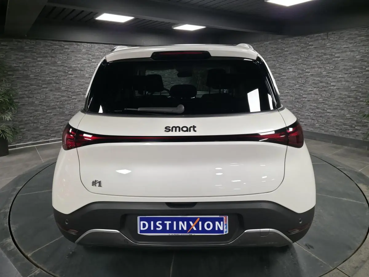 Vue arrière d'une Smart #1 blanche électrique 2024 avec feux arrière reliés par une bande lumineuse rouge.