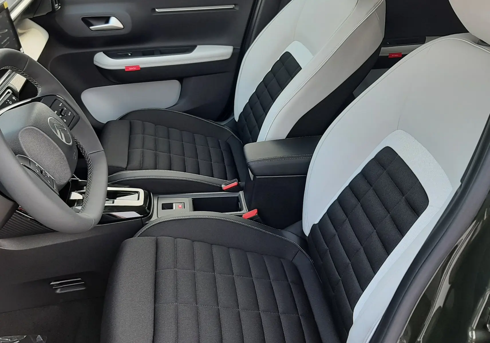 Vue intérieure côté conducteur de la Citroën C3 Aircross hybride 2026, sièges bicolores noir et blanc avec console centrale.