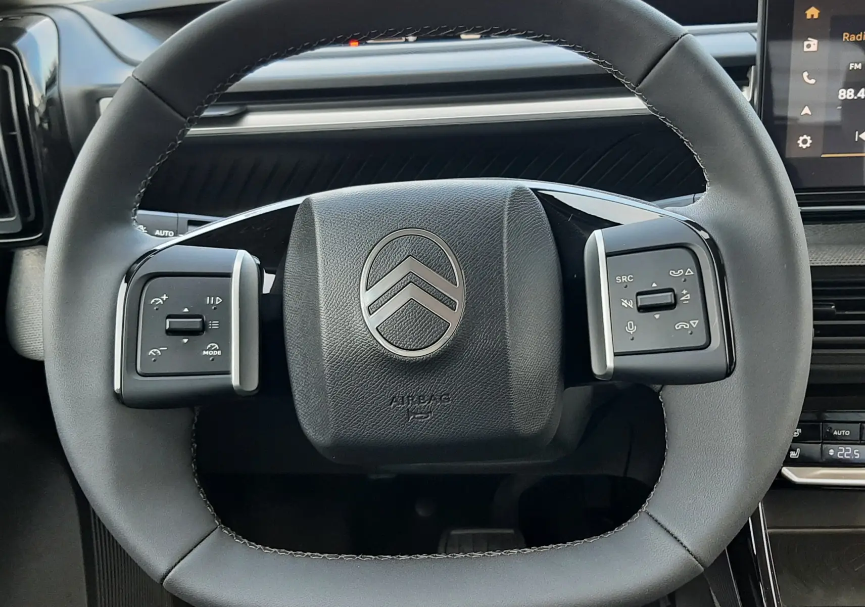 Vue rapprochée du volant noir au design carré de la Citroën C3 Aircross hybride 2026, avec commandes intégrées.