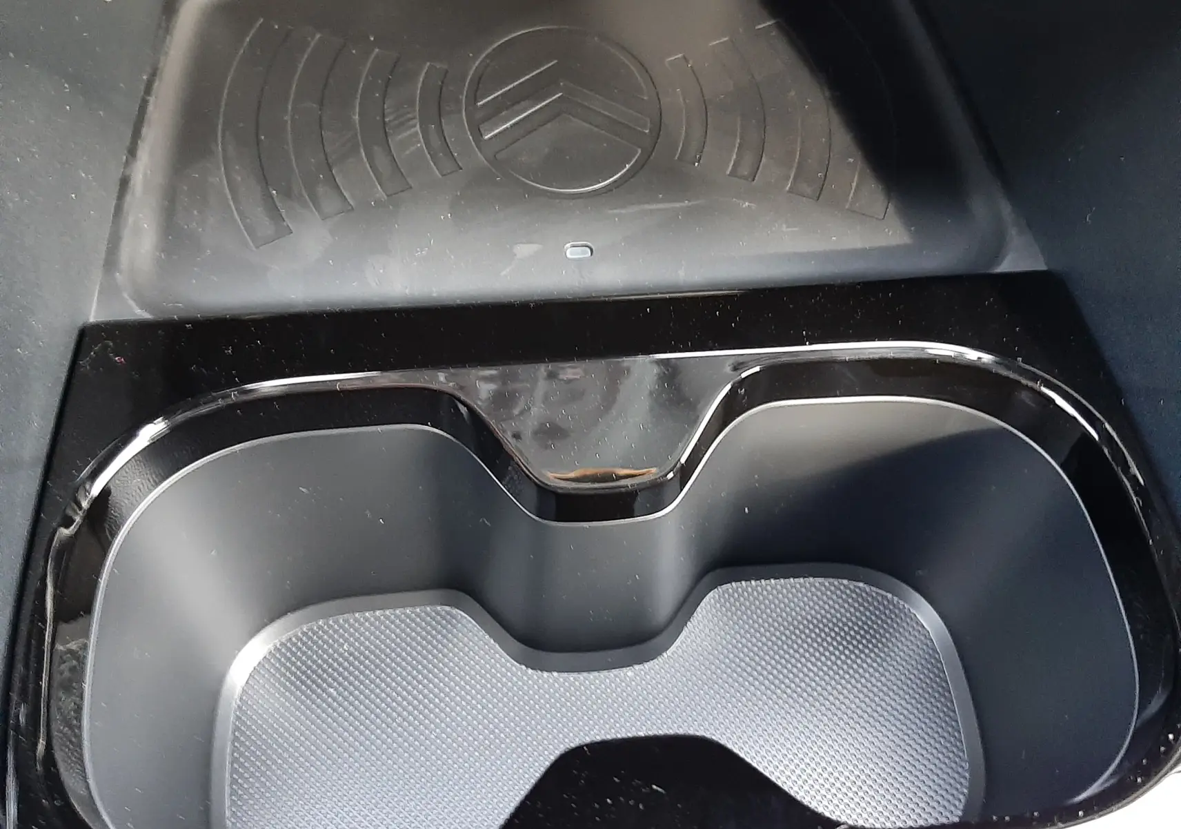 Gros plan sur le porte-gobelets noir et le chargeur à induction avec logo Citroën dans l'habitacle du C3 Aircross hybride.