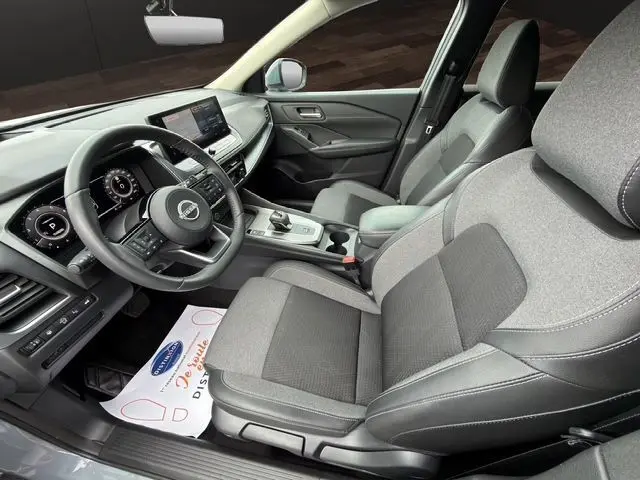Vue intérieure côté conducteur du Nissan Qashqai 2025 en gris céramique, avec tableau de bord digital et sièges tissu gris.