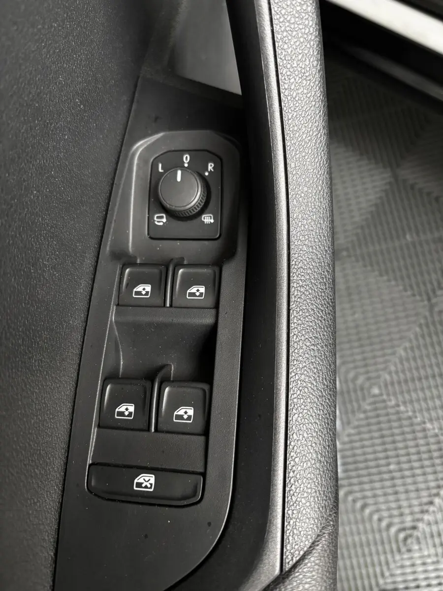 Gros plan sur les commandes noires des vitres électriques et rétroviseurs côté conducteur d'un Skoda Karoq noir 2025.