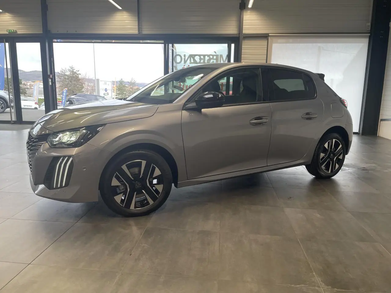 Peugeot 208 gris Artense vue de profil côté gauche en intérieur, avec jantes alliage bi-tons et feux LED 3 griffes.
