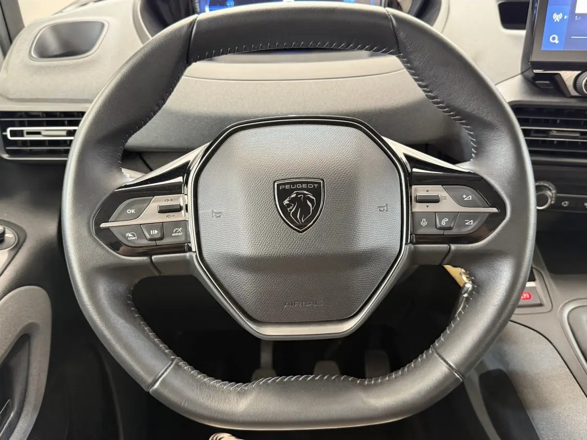 Vue rapprochée du volant cuir multifonctions noir du Peugeot Rifter 2024, avec commandes intégrées visibles.