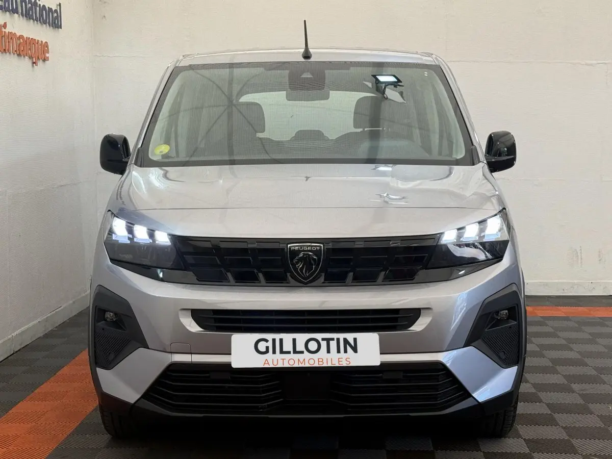 Vue frontale d'un Peugeot Rifter gris clair 2024 avec phares LED allumés et calandre noire distinctive.