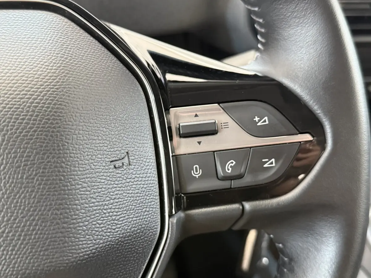 Gros plan sur le volant cuir multifonctions du Peugeot Rifter 2024, boutons de commande audio et téléphone visibles.