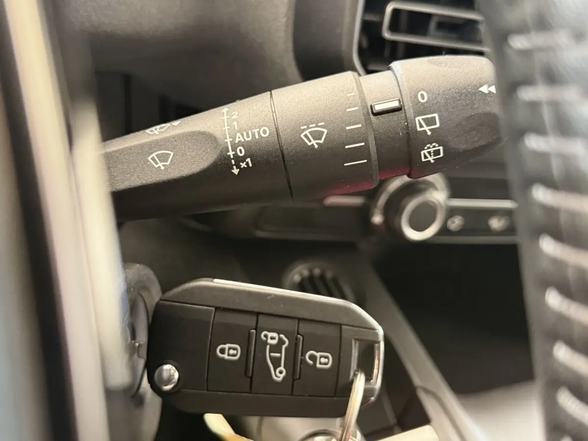 Gros plan intérieur sur la commande des essuie-glaces et la clé de contact du Peugeot Rifter gris clair 2024.