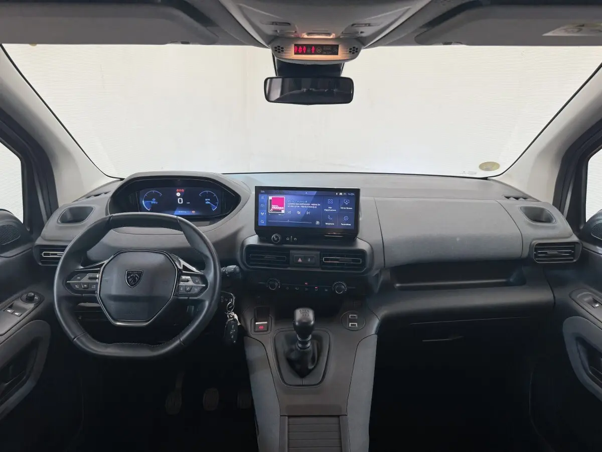 Vue intérieure frontale du tableau de bord gris du Peugeot Rifter 2024 avec volant cuir multifonctions et écran tactile central.