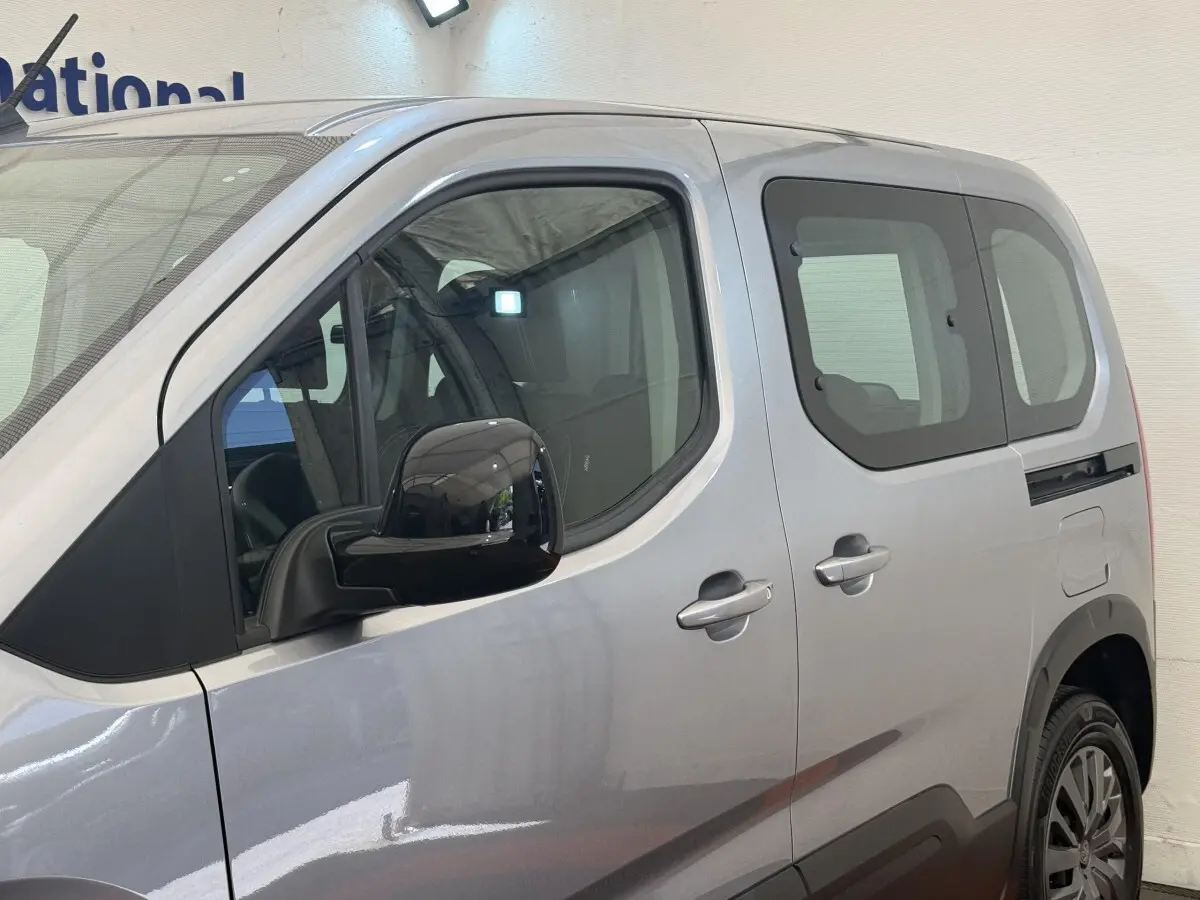 Vue côté gauche en gros plan sur le Peugeot Rifter gris clair, mettant en valeur la porte arrière coulissante et le rétroviseur noir.