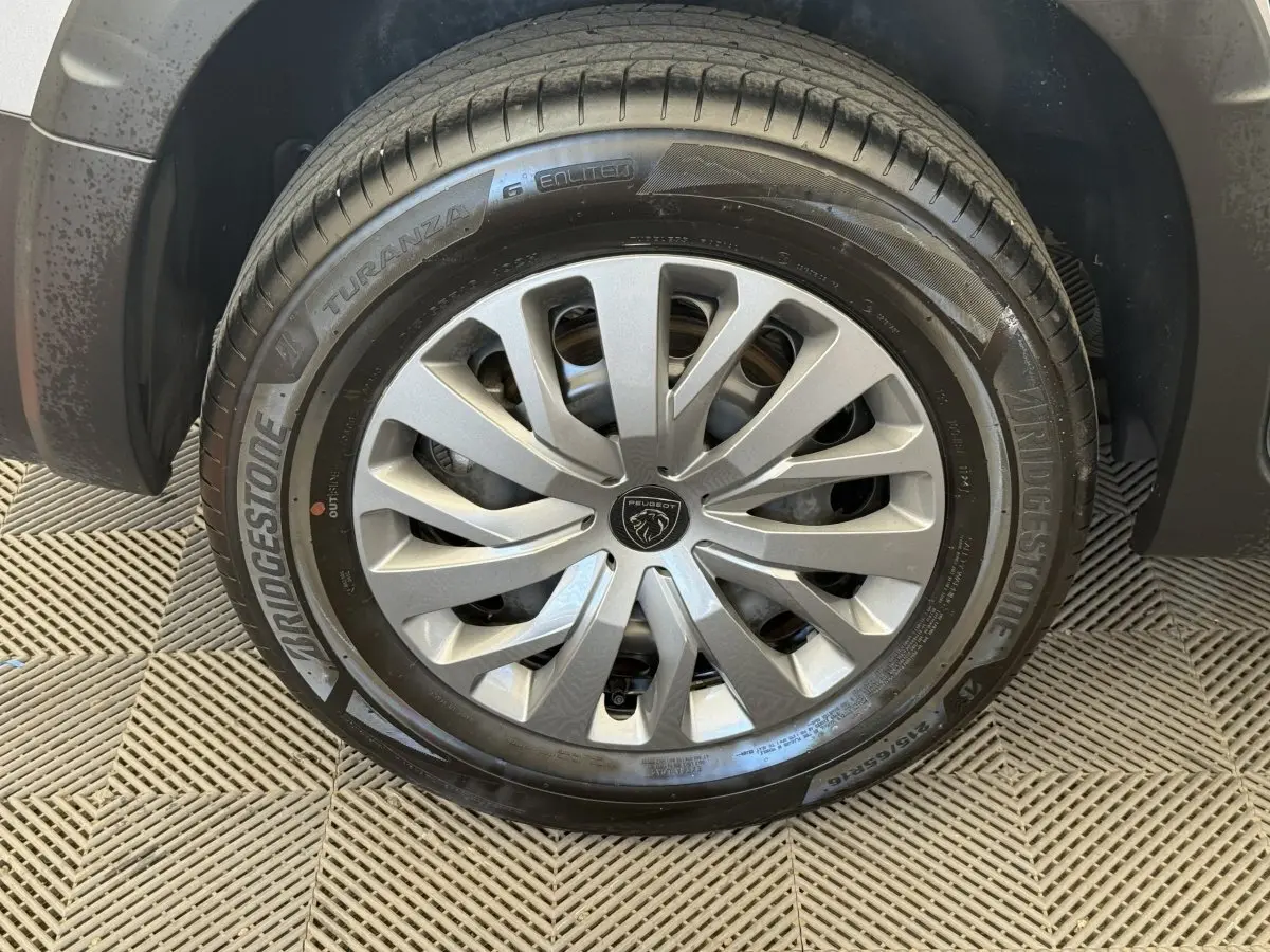 Gros plan sur la roue avant droite du Peugeot Rifter gris clair, avec jante à enjoliveur argenté et pneu Bridgestone.