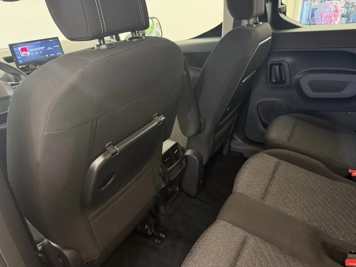 Vue intérieure arrière du Peugeot Rifter gris clair 2024, montrant les sièges tissu et tablette rabattable au dos des sièges avant.