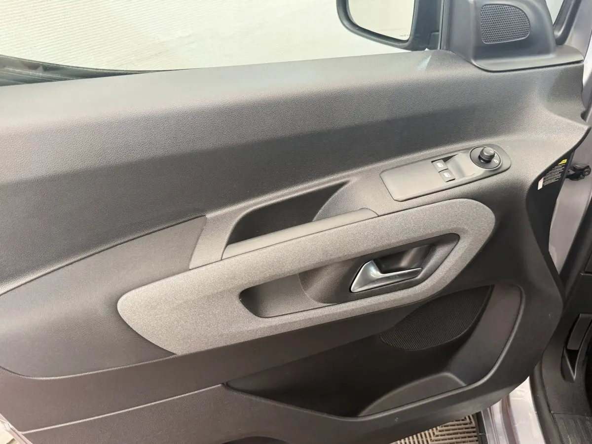 Gros plan sur la porte avant gauche du Peugeot Rifter gris clair 2024, avec commandes électriques et poignée intégrée.
