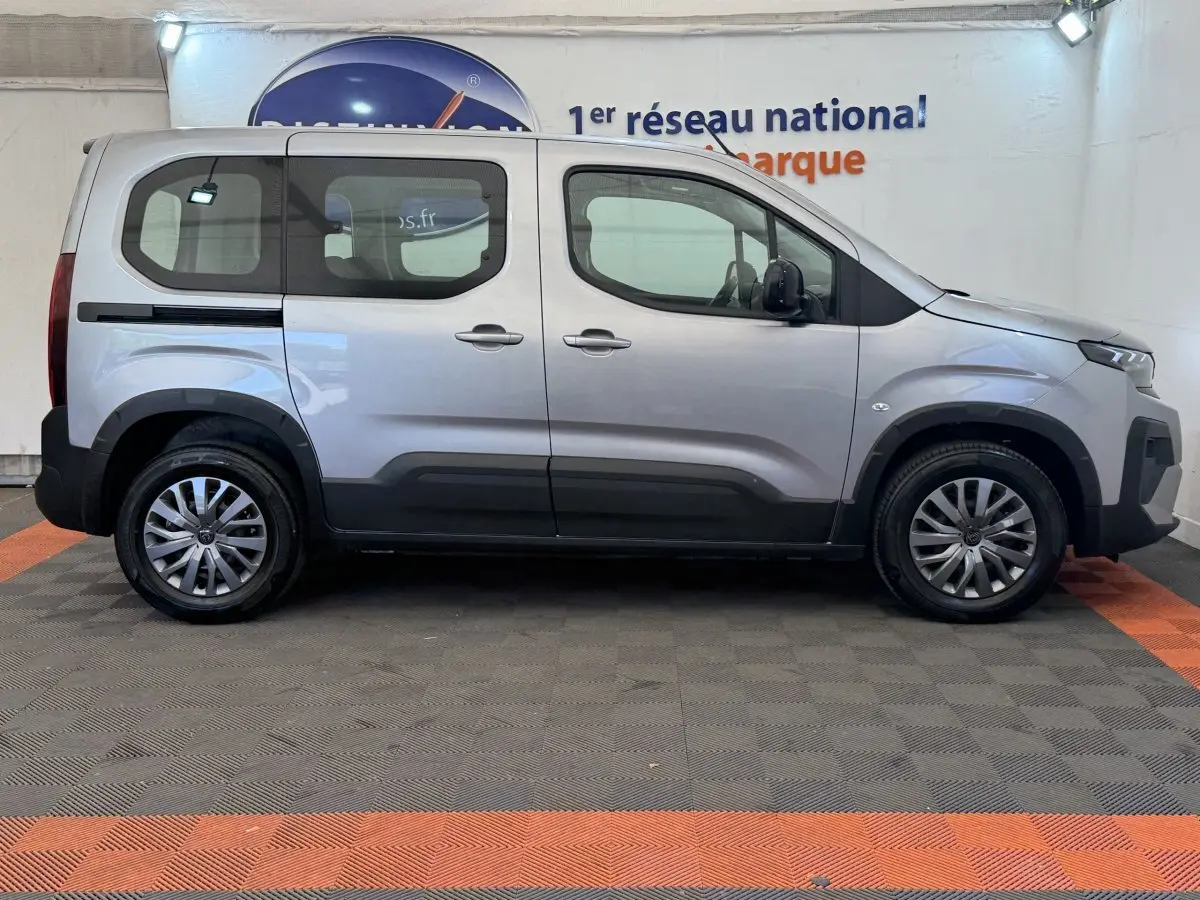 Vue de profil côté gauche d’un Peugeot Rifter gris clair 2024 avec vitres arrière teintées et jantes alliage.