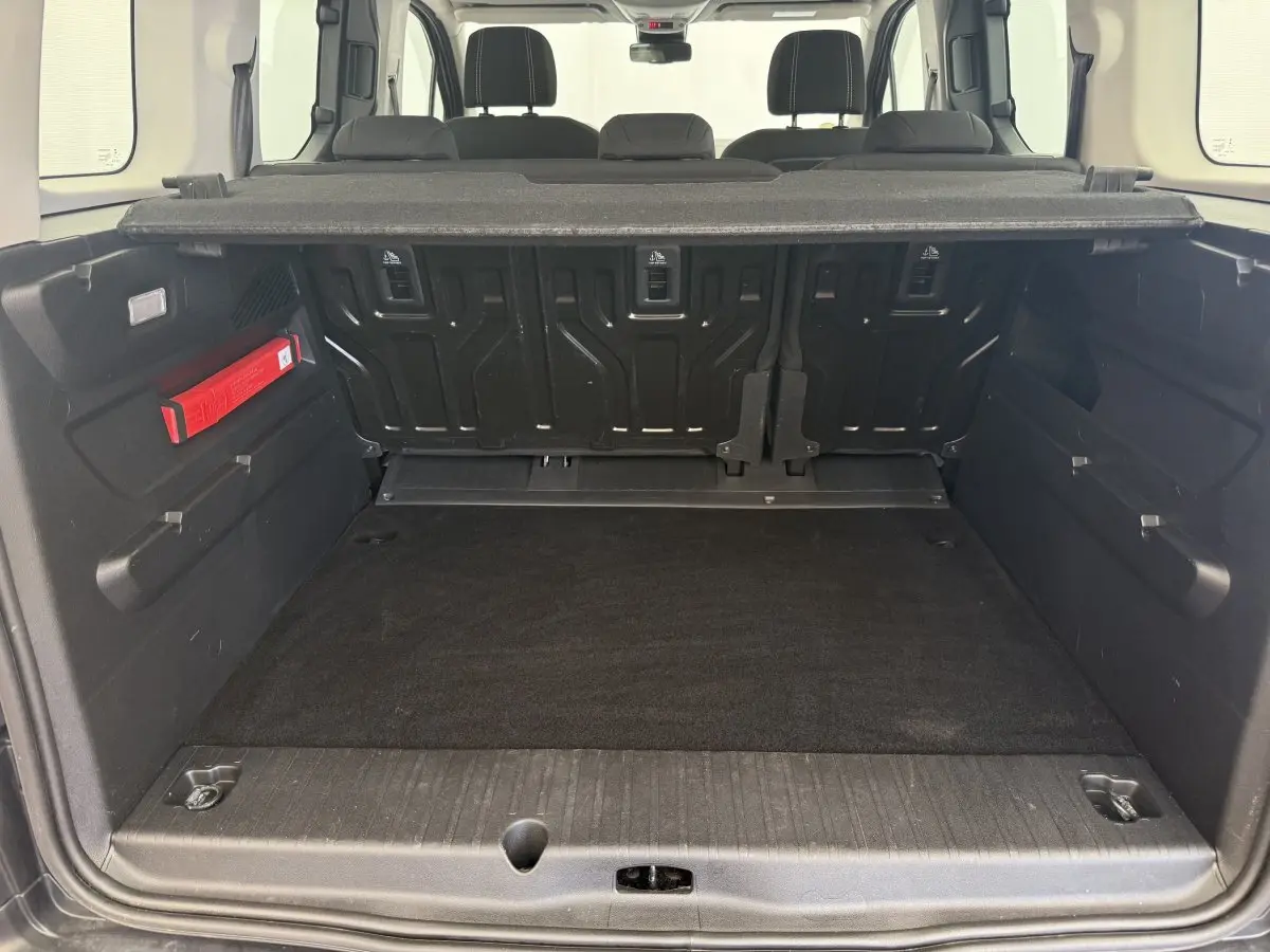 Coffre ouvert vu de l'arrière d'un Peugeot Rifter gris clair avec banquette arrière et cache-bagages visibles.