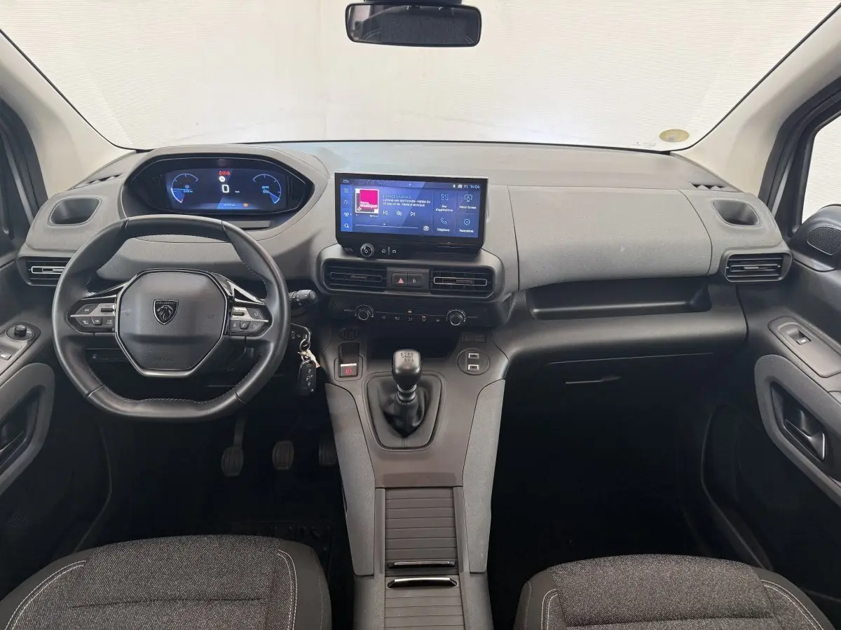 Vue intérieure avant du Peugeot Rifter 2024, tableau de bord moderne avec écran tactile central et volant cuir multifonctions.