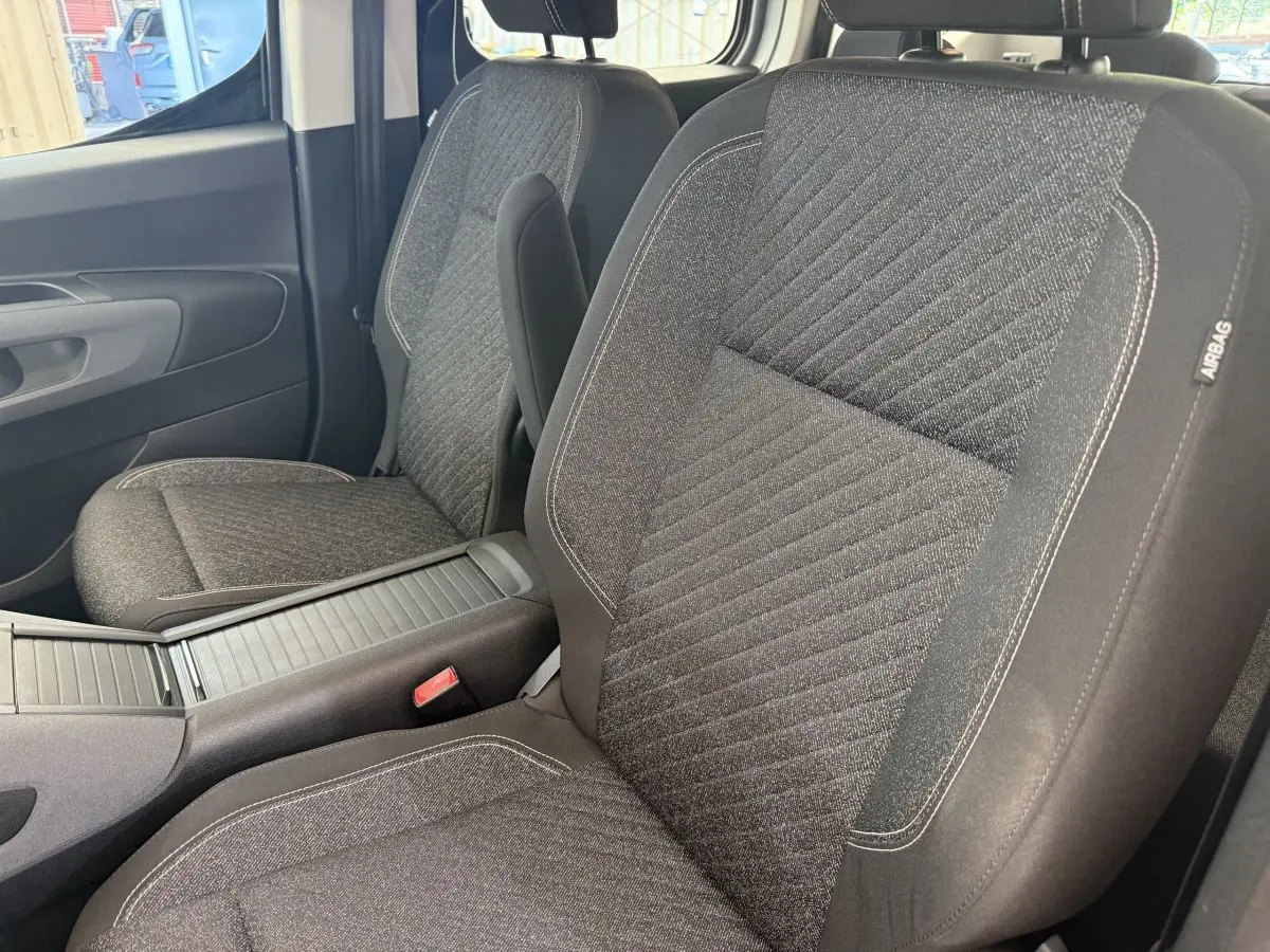 Vue rapprochée des sièges avant gris foncé du Peugeot Rifter 2024 avec accoudoir central et étiquette airbag.