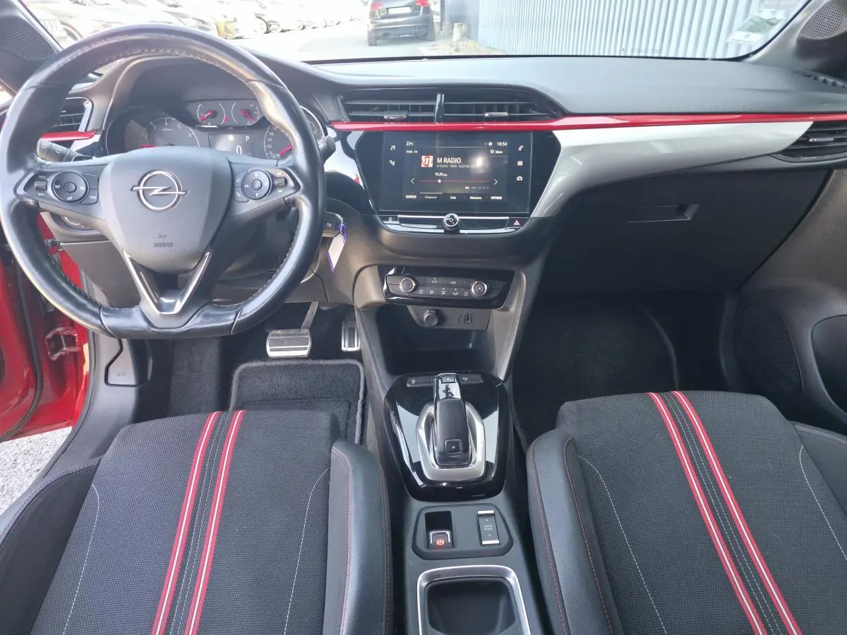 Vue intérieure avant de l’Opel Corsa rouge 2020, avec volant cuir, écran tactile central et sièges sport noirs à bandes rouges.