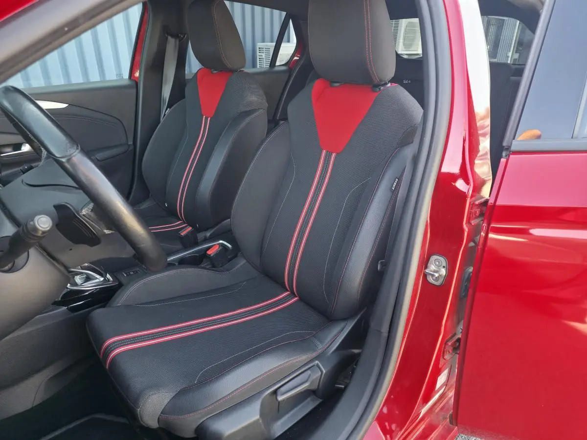 Vue intérieure côté conducteur d'une Opel Corsa rouge, sièges sport noirs avec surpiqûres et inserts rouges.