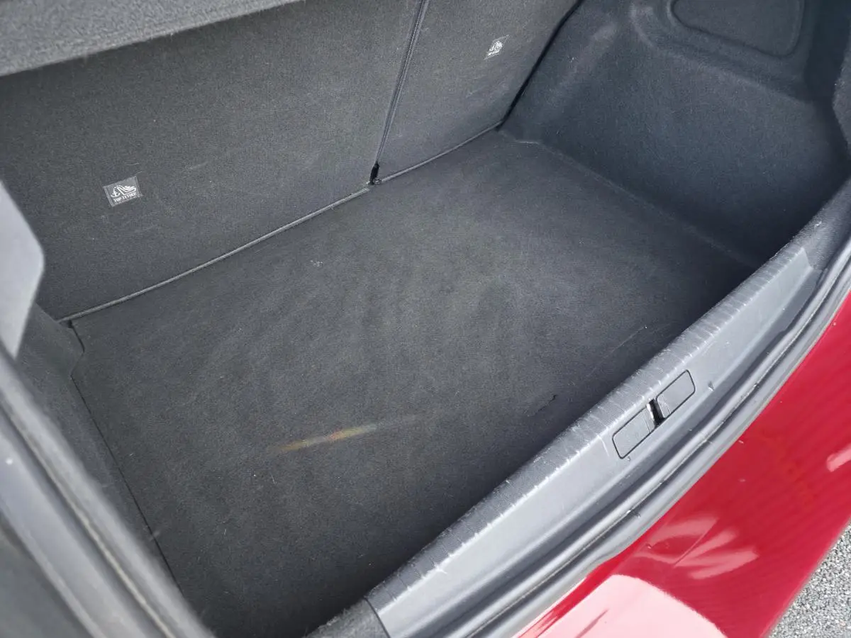 Coffre ouvert vu de dessus d’une Opel Corsa rouge, montrant le tapis de sol noir et l’intérieur spacieux.
