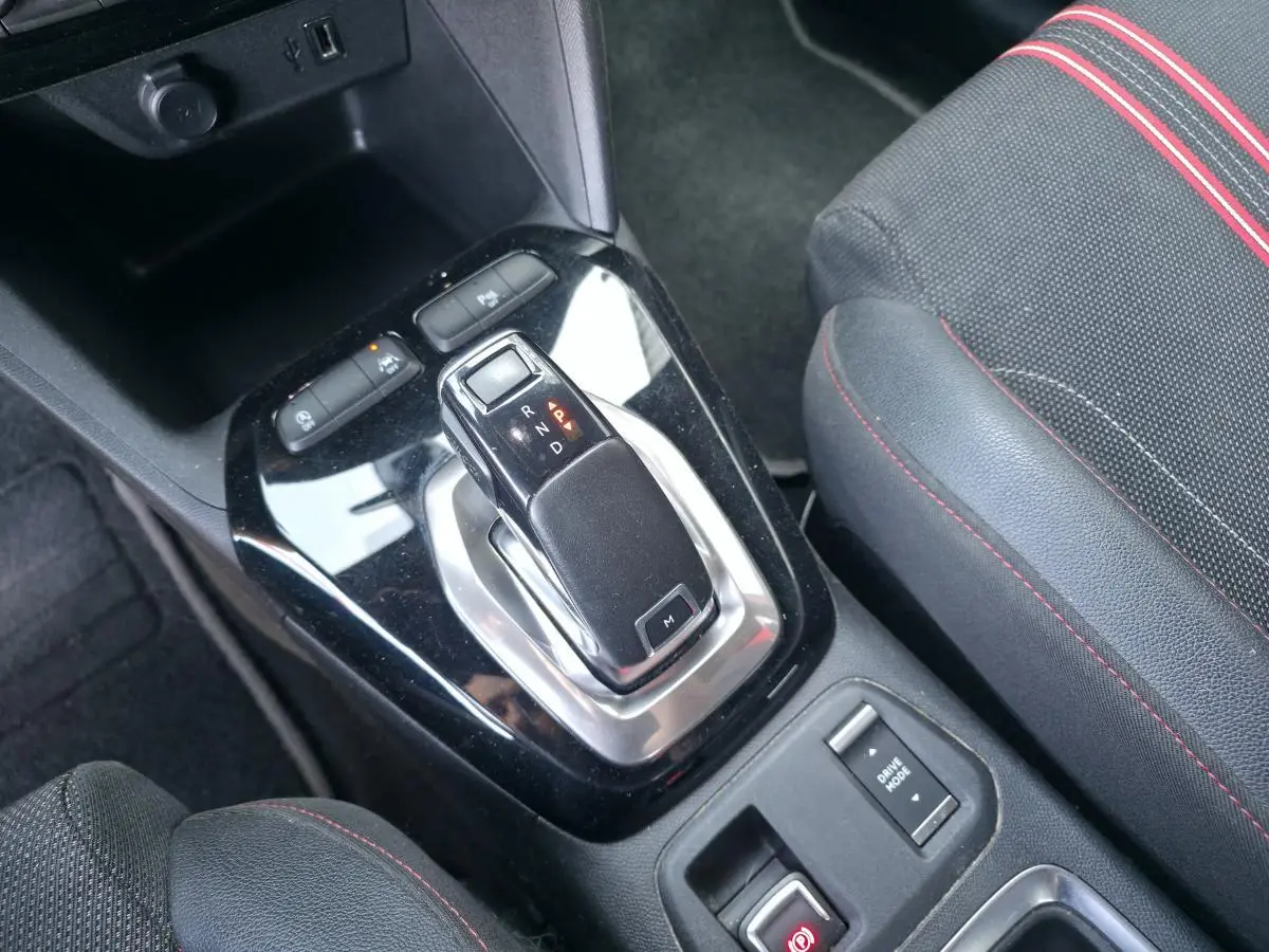 Gros plan sur la console centrale noire brillante de l'Opel Corsa rouge, avec levier de boîte auto et bouton mode conduite.