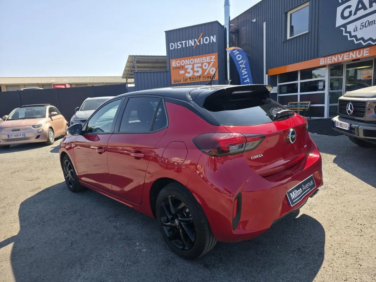 Opel Corsa rouge 3/4 arrière droit avec toit noir brillant et jantes alliage noires visibles.