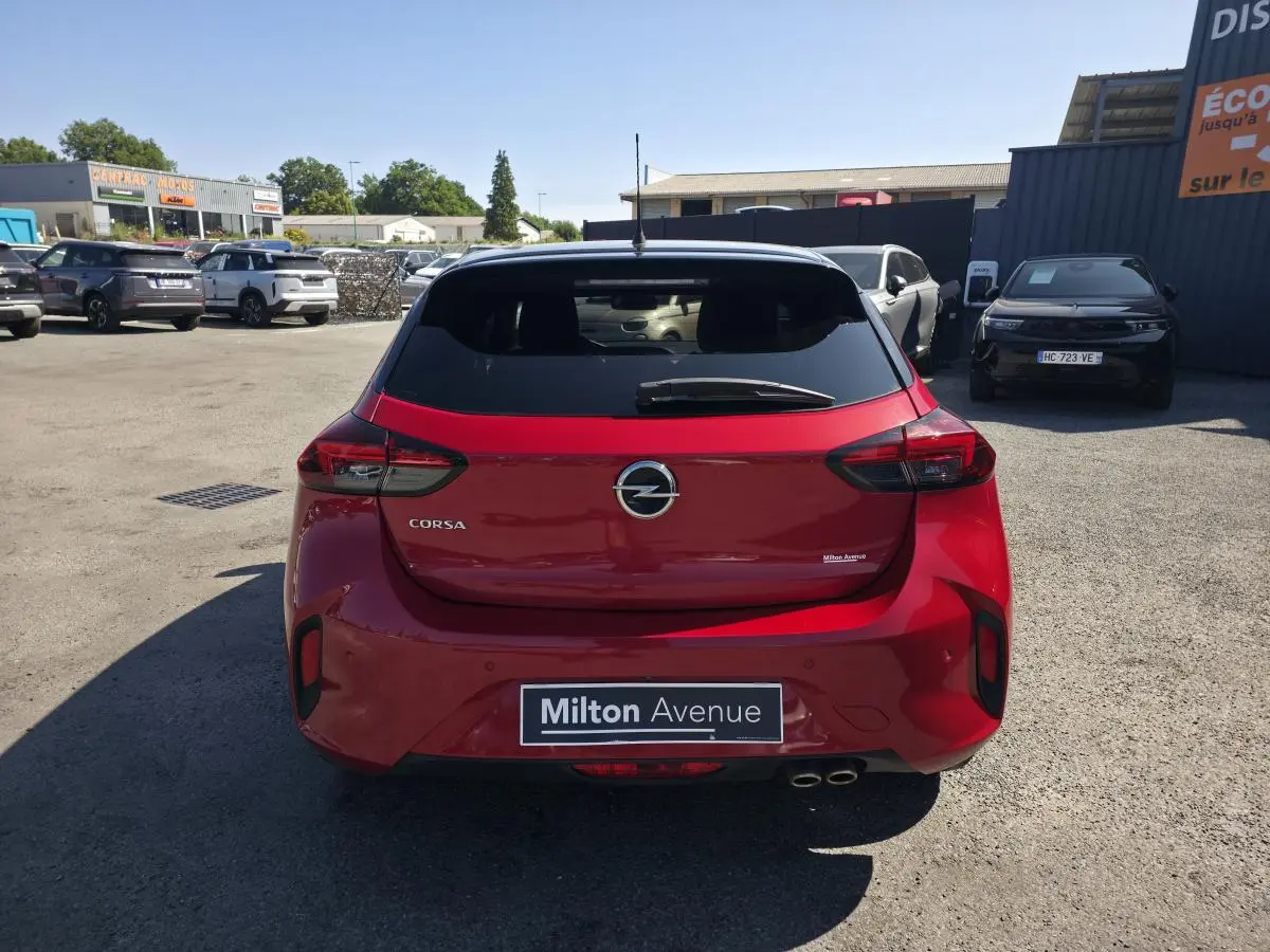 Vue arrière d'une Opel Corsa rouge 2020 avec toit noir et double sortie d'échappement chromée, stationnée en extérieur.